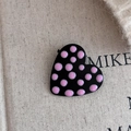 Vista dettagliata del fermaglio a cuore nero con finitura in smalto a pois rosa - Stile a pois cuore nero