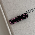 Dettaglio di un fermaglio per capelli nero in metallo con pois rosa su sfondo lino - Stile a pois ondulato quadrato cavo