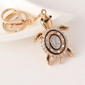 Sparkling gold turtle keychain with rhinestone shell on a white ceramic tray - Black