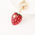 Sparkling strawberry keychain with red crystals and gold metal clasp on a white plate - Red