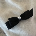 Elegant black fabric bow hair clip with central white pearl on a cream textured background - Black Bow Pearl