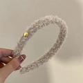 Dettaglio di un cerchietto in morbido peluche beige con un bottone dorato decorativo - Bianco Sporco