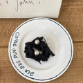 Elegante coletero de satén negro con tres grandes perlas artificiales en un plato de loza - Coletero de Perlas Negras