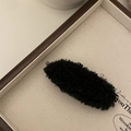 Close-up of a black plush lamb wool hair clip featuring soft texture and oval design - Black