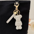 Sparkly white rhinestone bear keychain with gold clasp on black canvas bag - White