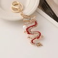 Golden Chinese dragon keychain with red rhinestones and a white pearl on white dish - Red