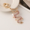 Golden dragon keychain with pink rhinestones and pearl accent on white background - Pink