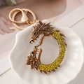 Golden dragon keychain with orange and green rhinestones in a white ceramic dish - Yellow