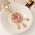 Porte-clés attrape-rêves doré orné de strass roses et breloques sur une assiette - Goutte d'eau Carrée Rose