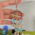Süßer goldener Katzen-Schlüsselanhänger mit Kristallen und blauem Emaille-Detail in der Hand - Blau