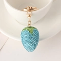 Detailansicht eines blauen Erdbeer-Schlüsselanhängers mit Strass auf weißer Keramiktasse - Blau