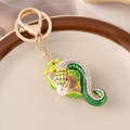 Golden snake keychain with green enamel and sparkling crystals on a white plate - Green
