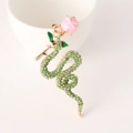 Llavero de serpiente dorada con rosa de esmalte y cristales verdes sobre fondo cerámico - Verde