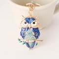 Portachiavi gufo blu con strass su ramo dorato accanto a una tazza di ceramica - Blu Reale