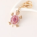 Golden turtle keychain with pink and purple rhinestones on white background - Pink