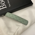 Gros plan d'une pince à cheveux en similicuir vert avec surpiqûres losanges sur soie - Vert