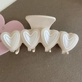 Close-up of beige heart-shaped claw clip with glossy finish on a textured background - Cream White Heart With White Edge