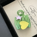 Primer plano de pinza para el cabello verde con estrella púrpura y corazón amarillo en tarjeta - Pinza Ovalada Verde Con Corazón Amarillo