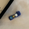 Detail van een blauwe gebreide haarklem met drie gekleurde strassteentjes op beige textuur - Donkerblauw