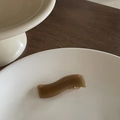 Dettaglio macro di un fermaglio per capelli ondulato in resina ambrata su un piatto di ceramica - Grigio Onda (7#)