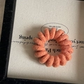 Macro detail of a coral orange spiral hair tie with a soft knitted wool texture - Orange