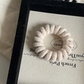Macro detail of cream spiral fabric telephone cord hair tie on a jewelry display board - Off-white