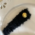 Detalle de pinza para el pelo de felpa negra con carita sonriente dorada en bandeja - Pinza de Pelo Negro (Cara Sonriente)