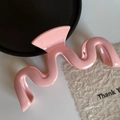Vue rapprochée d'une pince à cheveux rose ondulée au fini brillant sur fond de carte décorative - Rose