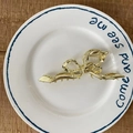 Polished gold metal bow-shaped hair claw clip with ribbed texture on white ceramic plate - Bow / Gold Bowknot Style
