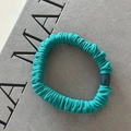 Detalle de un coletero de tela plisada verde azulado con una cuenta ovalada de resina azul - Verde