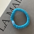 Detalle de un coletero de tela plisada azul con una cuenta decorativa azul claro - Azul