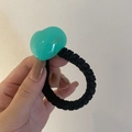 Detail of mint green acrylic heart charm on a black braided hair tie with gold text - Blue Heart