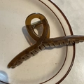 Close-up of a 14cm amber acrylic hair claw clip with cross-twist design on ceramic plate - Khaki Cross