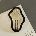Detailed close-up of a wavy black and gold cloud-shaped hair clip on a display card - Black