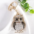 Golden owl keychain with glasses and white crystals on a white ceramic tray - Black