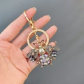 Portachiavi ape dorata con strass viola e grigi tenuto in mano su uno sfondo azzurro - Viola