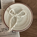 Dettaglio di un fermaglio per capelli crema a forma di fiocco su un vassoio con giornali - Clip a Fiocco Bianco Latte