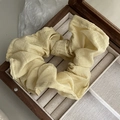 Detailed macro shot of textured pale yellow waffle fabric scrunchie in a wooden tray - Yellow