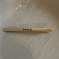 Dettaglio del fermaglio dorato Smile con scritte incise e icona smile su fondo avorio - Fermaglio per Capelli con Faccia Sorridente Oro