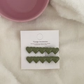 Close-up of two olive green heart-shaped hair clips on white card packaging over soft fabric - Dark Green Heart