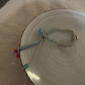 Detail of hand-woven ethnic bracelet with colorful beads and small gold bell on ceramic tray - Blue (Blue Rope Bracelet)