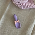 Detail einer lila Schleifen-Haarklammer auf beigem Stoff mit rosa Dekoelementen - Lila