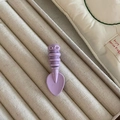 Close-up of a purple candy-colored spoon hair clip on a beige striped fabric display case - Purple