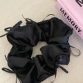 Detail of black satin hair scrunchie with delicate bow ribbons on cream textured background - Black