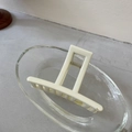 Detailansicht einer mattbeigen minimalistischen Haarklammer mit Kreuzdesign auf Glas - Cremeweiße Leiste