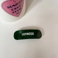 Gros plan d'une barrette en acétate vert marbré avec le logo LAYMOOD blanc sur fond blanc - Arc Vert