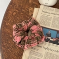 Dettaglio di un elastico per capelli a quadretti rosa e marroni su legno e giornale - Scrunchie Plaid Rosa Caffè