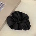 Close-up of elegant black satin scrunchie showing glossy fabric texture and soft pleats - High-end Minimalist Style / Black