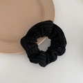 Detailed view of black knitted scrunchie showing ribbed texture on a beige ceramic plate - Black
