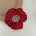 Detailed view of red knitted scrunchie with thick ribbed texture on ceramic plate - Red